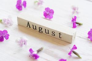 top view of wooden calendar with August sign and pink flowers. photo