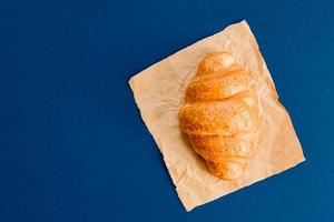 top view of croissant on craft paper on blue background with copy space. photo