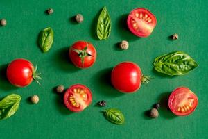 Halved Juicy Cherry Tomatoes and Basil Leaves on a green background. Concept for healthy nutrition. Top view. Copy space. photo