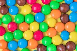 Colorful Background of multicolored sweet candies. Round bonbons scattered on yellow background photo