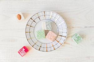 Traditional turkish delight on a plate on white wooden background. Assorted Oriental sweets. Top view. photo