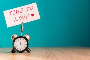 Alarm clock and banner with handwritten phrase time to love on wooden table. Vacation concept. Toned photo