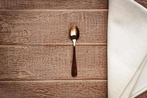 Top view of cloth napkin of beige color and served tea spoon on wooden table. photo