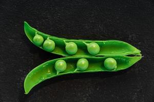 Vegetable backdrop vith copy space for your projects. Close up of fresh ripe green peas on black background photo