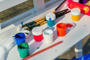 Artist's work place. Open multicolored gouache, paint brushes and pencil on white table. photo