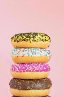 Stack of glazed sweet doughnuts with sprinkles and nuts on pink background. Copy pace for your text photo