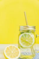 Citrus lemonade water with sliced lemon and mint, healthy and detox water drink in summer on yellow background. Summer bright backdrop with copy space photo