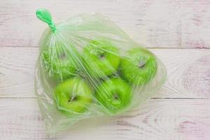 Fresh green apples in plastic bag on wooden table. environmental concept of non-ecological use of plastic photo