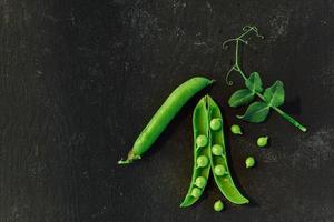 telón de fondo vegetal con espacio de copia para sus proyectos. Cerca de guisantes verdes maduros frescos sobre fondo negro foto