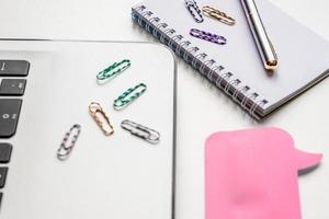 close up of empty spiral notepad, silver pen, pink sticker and laptop on white background. Business or education concept photo