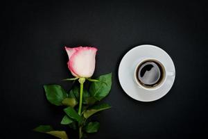 Cup of black coffee and pink rose on black background, Top view, copy space. photo