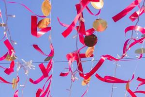 red festive ribbons and gold circles against blue sky. Colorful garland for event decoration