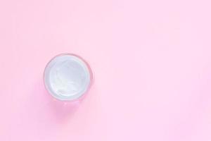 glass jar with face or body cream on pastel pink background with copy space. Top view, flat lay. photo