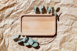 Wooden tray on pastel beige paper craft background. Card mockup. Elegant floral wedding layout. Eucalyptus branches. Minimal eco template. Aesthetic interior. Wood oak tray. Eucalyptus leaves photo