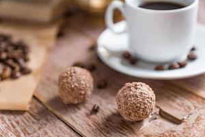 pausa para el café. taza de café turco recién escrito, bolas de chocolate y libro sobre mesa de madera foto