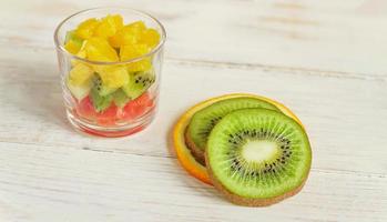 dieta ensalada de frutas mezcla fresca y sabrosa en un frasco de vidrio sobre una mesa de madera. naranjas jugosas picadas, kiwi y pomelos. foto