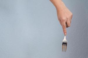 mujer mano sosteniendo tenedor sobre fondo gris. gesto de comer. foto