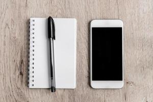 Business and office concept - blank notebook, smartphone and black pen on wooden table. Minimal flat lay, top view. photo