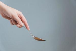 mano de mujer sosteniendo una cuchara sobre fondo gris. gesto de comer. foto