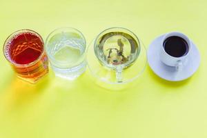 Top view of different beverages - drinking coffe, sparkling water, apple juice and green tea on yellow backgeound. Healthy life and diet concept photo