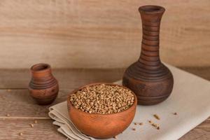 Dry buckwheat in brown clay bowl on wooden table. gluten free grain for healthy diet photo