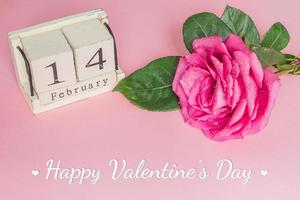 valentines day and holidays concept - close up of wooden calendar with 14th february date,  and pink rose on pink background photo