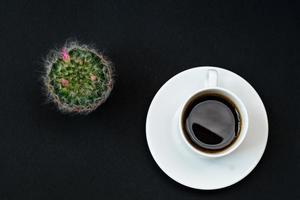 Cup of black coffee and blooming cactus on black background, Top view, copy space. photo