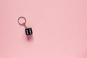 top view of black dice on key chain on pink background. Minimal flat lay concept photo