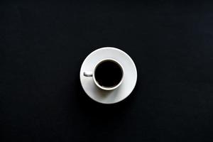 top view of white cup of coffee on black background. Minimal flat lay. photo