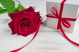 Beige polka dot gift box with red ribbon bow and bautiful red roses on wooden background. Greeting card for holiday. photo