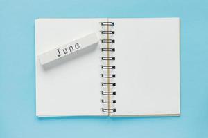 libreta de espiral limpia para notas y mensajes y barra de calendario de madera de junio sobre fondo azul. plano de negocios mínimo foto