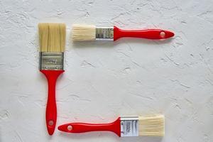 three paintbrushes with red handles on freshly made concrete background. Repairing concept. Top view with copy space photo
