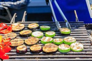 the chef cooks vegetables on grill. Slices of zuccini, eggplant, pepper roasted on open fire photo