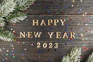 New Year's concept. Heppy new year 2023 wooden text on a wooden background, fur-tree branch on the edge of the frame photo