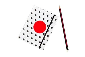 Black and white polka dot note book with red circle  on the cover and black pencil on white background. photo