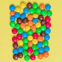 Colorful Background of multicolored sweet candies. Round bonbons scattered on yellow background photo