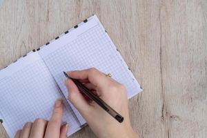 young woman hands hold opened notebook pages with black pen on  wooden table photo