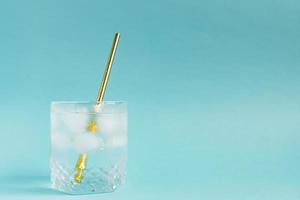 Close up of pure water with ice and paper straw in transparent glass and sun glare on blue background. photo