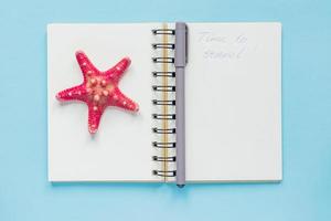 Top view of open empty notebook with starfish and time to travel inscription on pastel blue colorful background. Travel and holiday concept photo