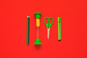 Creative flat lay of school supplies - green pens, pencils, scissors and hourglass on a red background photo