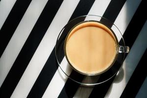 taza de café caliente con leche sobre un fondo de rayas blancas y negras. copie el espacio foto