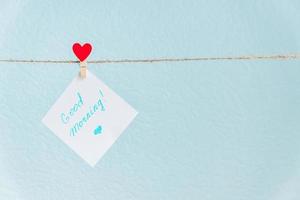 Pinned paper with good morning inscription hanged on cord against blue background photo