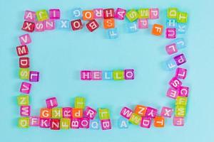 Multicolored plastic cube beads with letters scattered on blue background. English Alphabet background texture photo