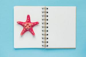 Top view of open empty notebook with starfish on pastel blue colorful background. Travel and holiday concept photo