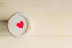 disposable craft paper coffee cup and red wooden heart on a cap. Coff to go on wooden table photo