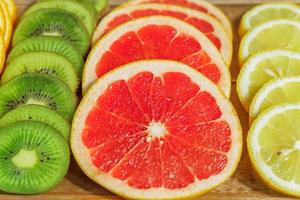 close up of slices of oranges, lemons, kiwi, grapefruit pattern on wooden background. photo