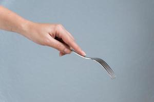 woman hand holding fork on gray background. Eating gesture. photo