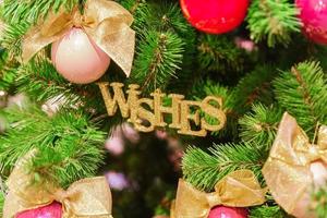 fondo de navidad y año nuevo. primer plano de las decoraciones de abetos: bolas de navidad rosas y rojas con arcos dorados y deseos de juguetes brillantes con forma de palabra foto