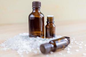 Pile of sea salt and bottles with aromatic essential oil on wooden table. Natural ingredients for spa and exfoliation. photo