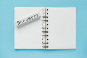 Clean spiral note book for notes and messages and december wooden calendar bar on blue background. Minimal business flat lay photo